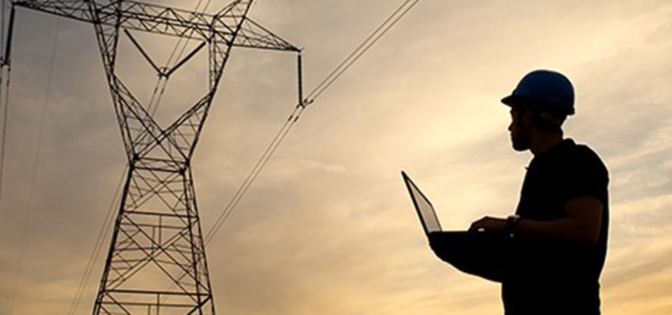 silhouette of a line worker looking at a transmission tower