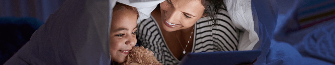 Mom and daughter under blankets looking at tablet