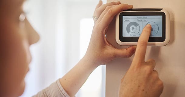 Woman touching her smart thermostat and reading how her energy consumption has gone down