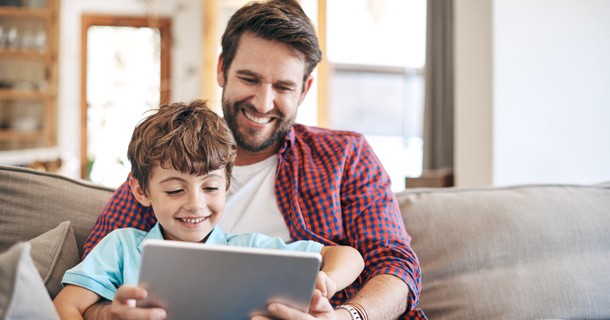 A father and son sitting together looking at a tablet 